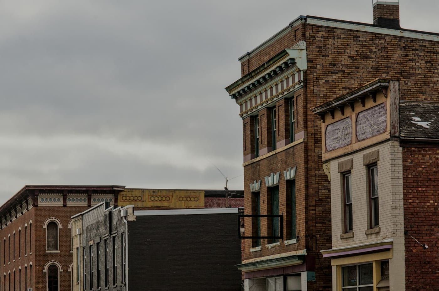 Upper floors of two- and three-story brick commercial buildings with painted cornices and arched windows, under an overcast sky