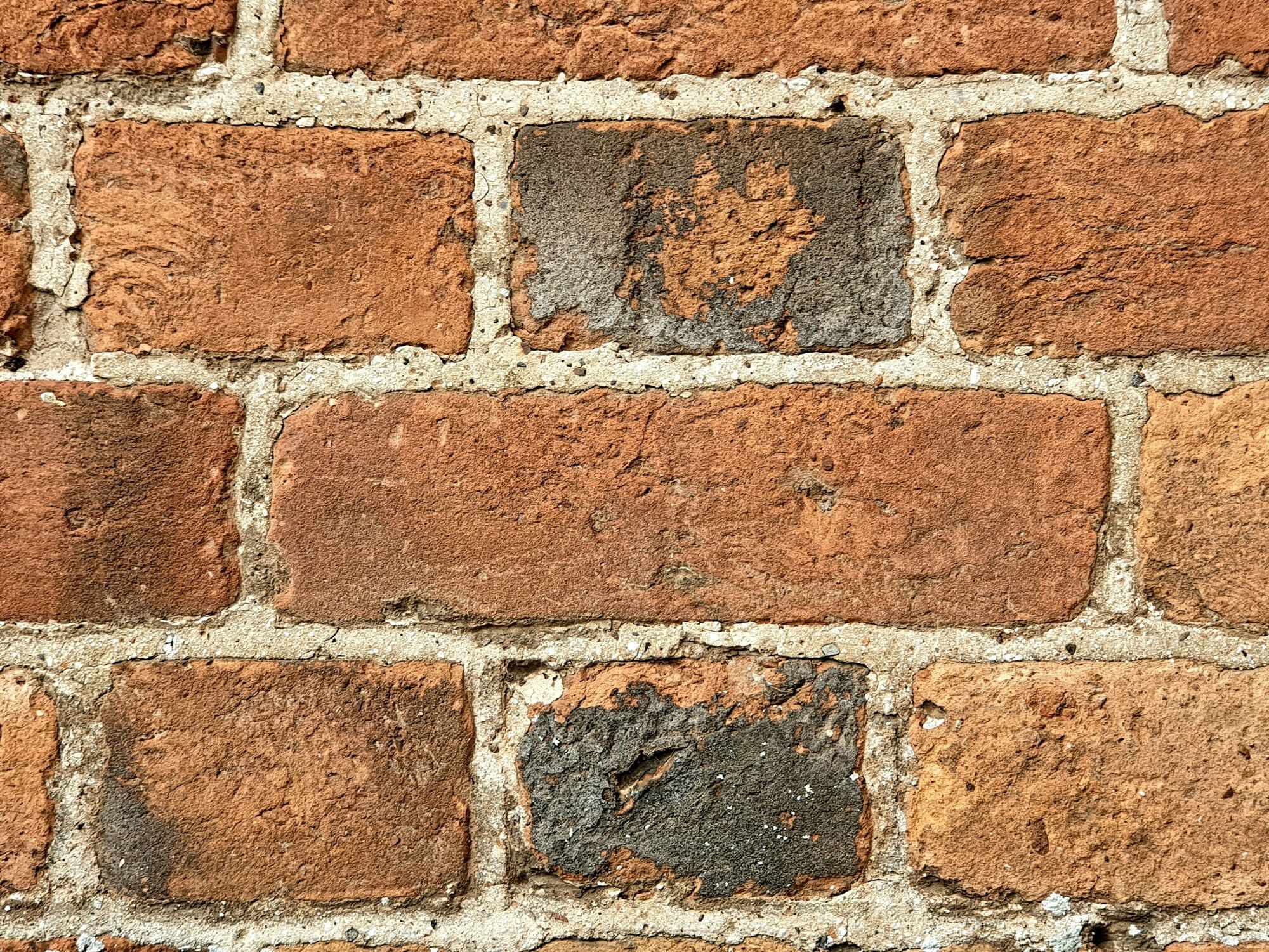 Close-up of old soft orange brick with sandy, eroded mortar joints that have weathered back unevenly from the brick faces