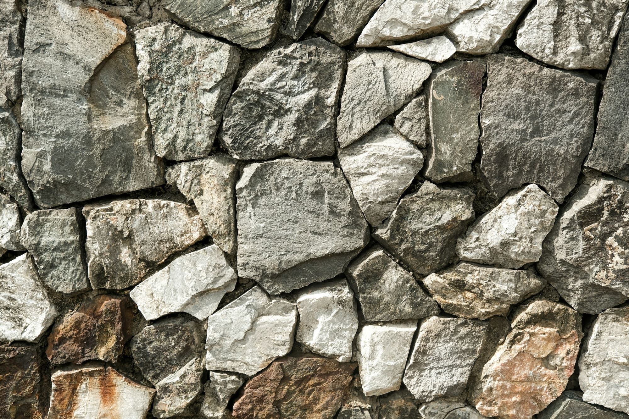 Wall of irregular natural stone in gray, white and rust tones, fitted together with recessed mortar joints