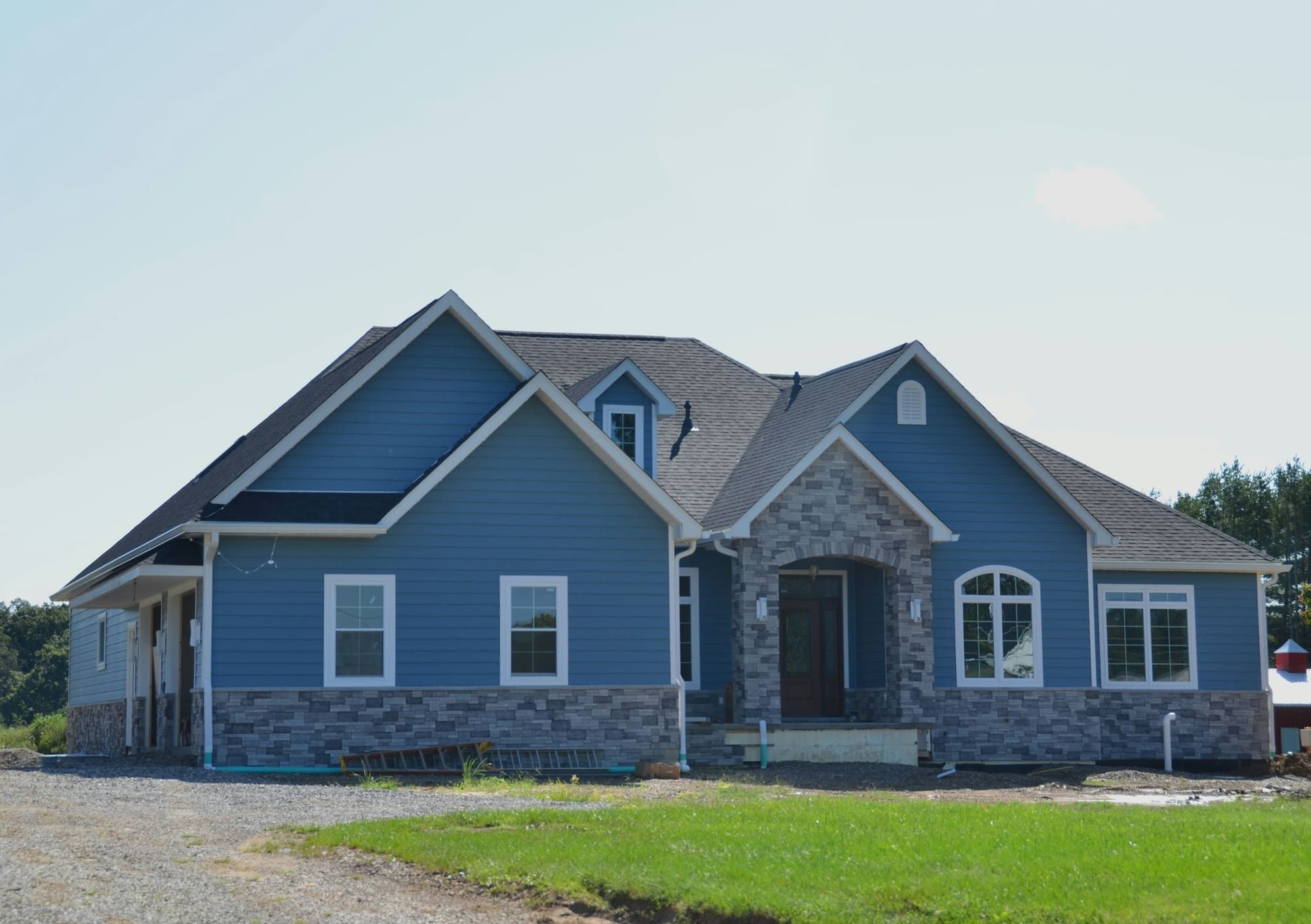 Newly built blue house with white trim and a gray stone veneer wainscot and entry surround, with the yard still unfinished