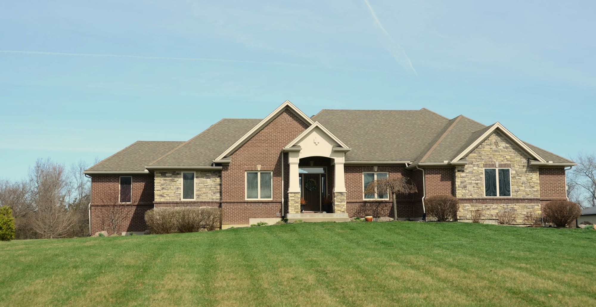 Newer ranch-style house with a red brick front and tan stone veneer around the entry and one gable, on a wide mowed lot