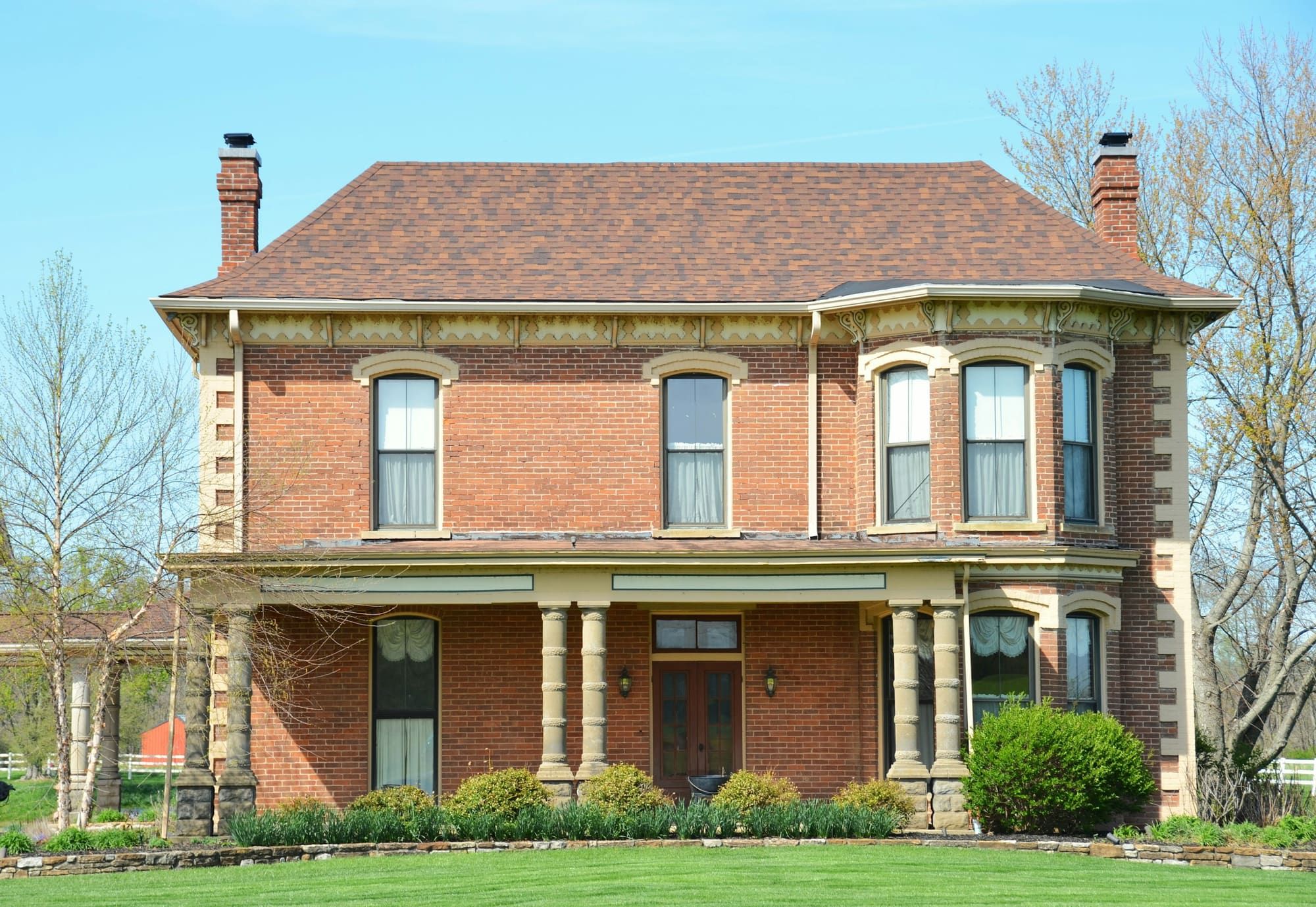 Two-story red brick house with pale stone quoins at the corners, arched window hoods, a columned front porch and a brick chimney at each end of the roof