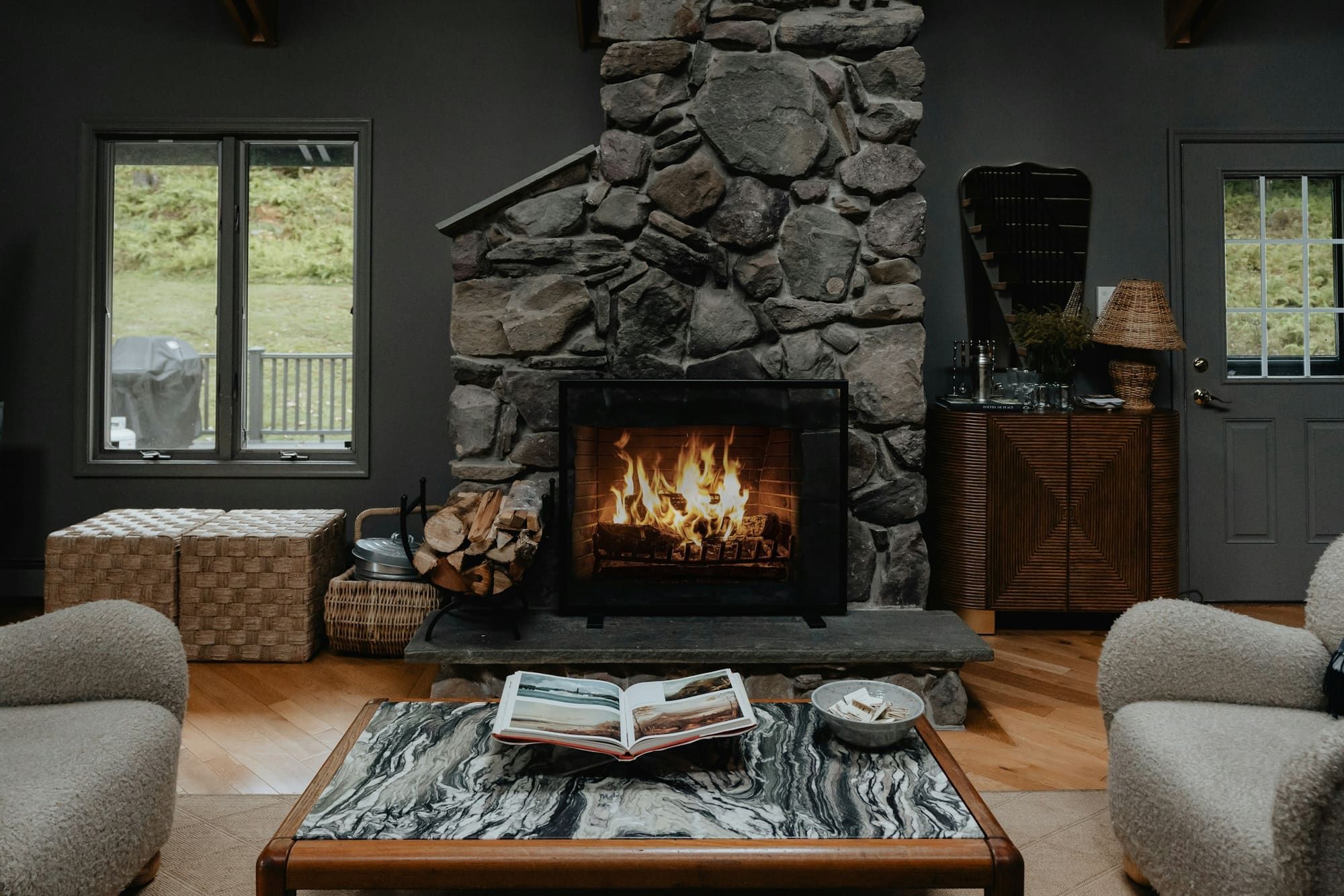 Living room with a floor-to-ceiling fieldstone fireplace and raised stone hearth, a fire burning behind a black screen