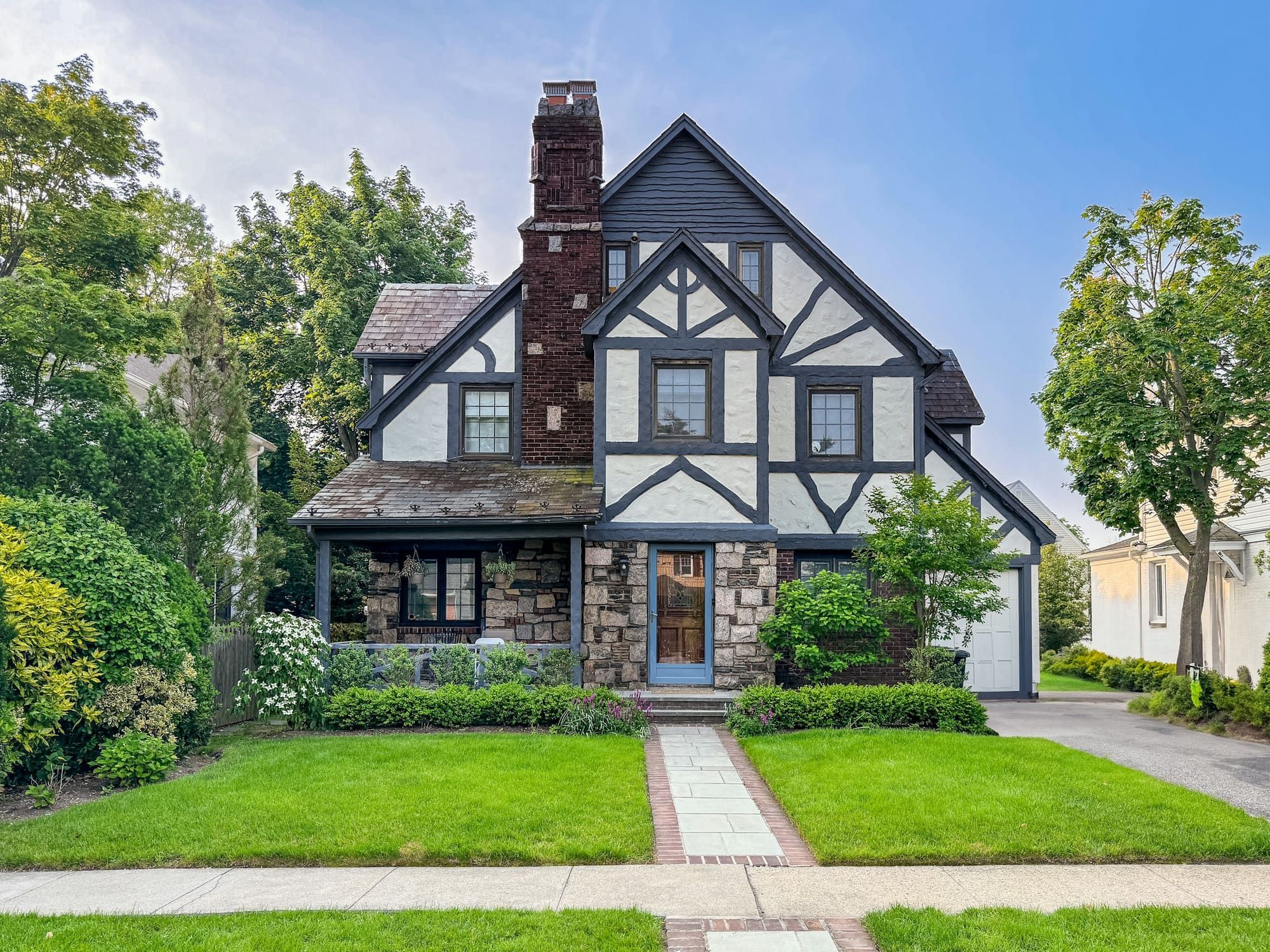 Tudor Revival house with cream rough-troweled stucco panels between dark half-timbering, a stone first story and a tall dark brick chimney